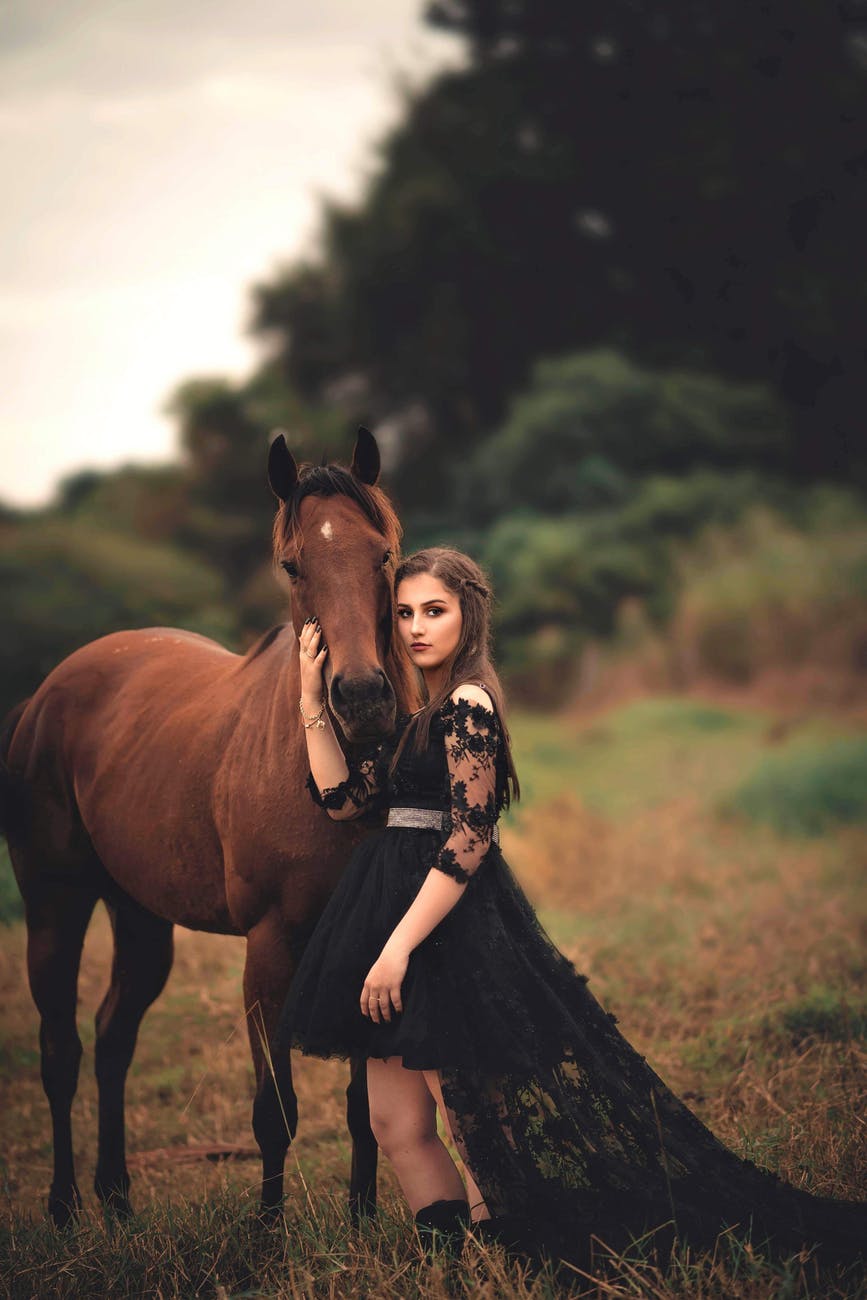 photo of woman wearing black dress beside horse